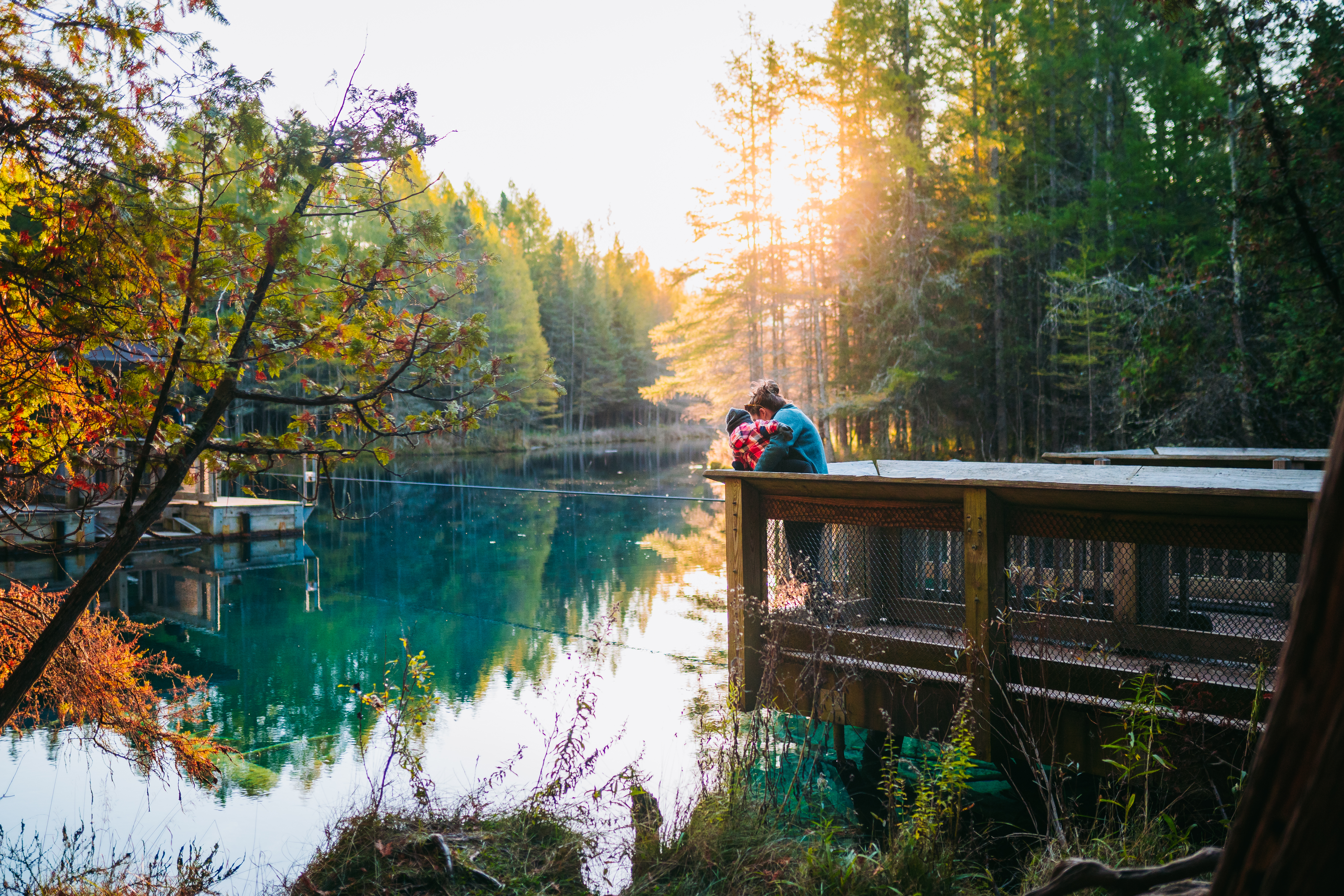 Kitch-iti-kipi in the Fall A woman holding a toddler on the dock at Kitch-iti-kipi spring